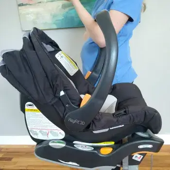 Person in blue shirt adjusts a black infant car seat base installed in a car.